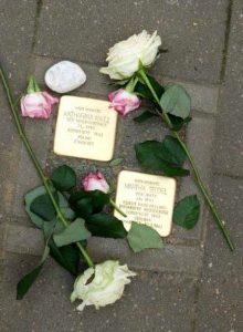 Zwei Stolpersteine mit Lebensdaten von Katharina Katz und Martha Stodel, daneben zwei weiße und drei rot-weiße Rosen sowie ein Kieselstein